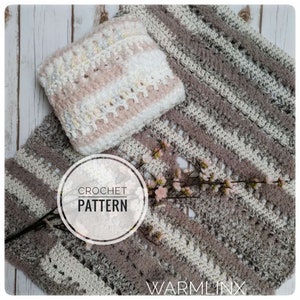 Puede incluir: Un patrón de crochet para una manta a rayas en tonos grises, blancos y rosas. El patrón incluye una pequeña almohada en los mismos colores. La imagen también incluye una rama de flores blancas y el texto "CROCHET PATTERN" y "WARMLINX".