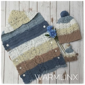 May include: A crocheted baby blanket with a hood, striped in blue, white, beige and brown. The blanket has buttons down the front and comes with a matching crocheted hat with a pom-pom on top. The blanket and hat are laid out on a white wooden surface. The text "WARMLINX" is visible in the bottom right corner of the image.