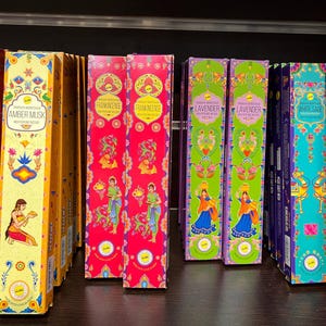 May include: Assortment of incense sticks in colorful packaging with various scents, including Rose, Amber Musk, Frankincense, Lavender, and White Sage. Each box features intricate designs and illustrations.