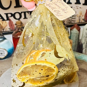 May include: A small, gold mesh bag filled with dried orange slices, herbs, and a handwritten tag that reads "Ostie Bot!  Smell My Bag!"