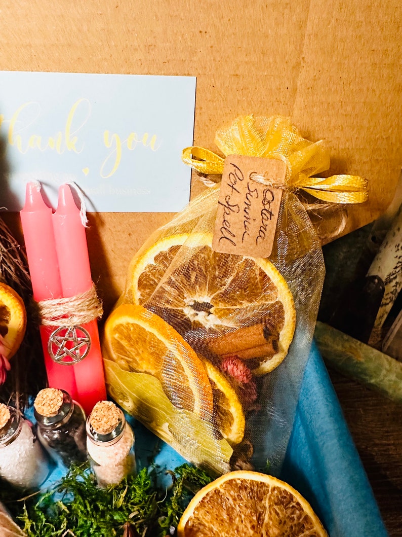 May include: A yellow organza bag filled with dried orange slices, cinnamon sticks, and pink flower buds. The bag is tied with a yellow ribbon and has a brown tag that reads "Autumn & Spice Spell".