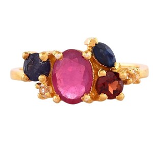 May include: A gold ring with a cluster of colorful gemstones. The ring features a large oval pink stone surrounded by smaller blue and red stones.
