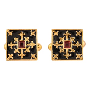 Può includere: Un paio di gemelli in oro con smalto nero e accenti di pietre preziose rosse. I gemelli presentano un design geometrico con una croce centrale.