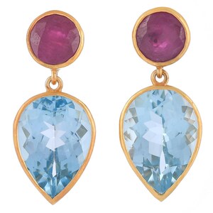 May include: A pair of gold-toned earrings featuring a round, deep pink gemstone at the top and a light blue, teardrop-shaped gemstone below. The earrings have a simple, elegant design.
