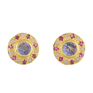 May include: A pair of gold-colored stud earrings. Each earring features a central, round, light blue gemstone surrounded by a ring of small, pink and white gemstones. The earrings are set against a white background.