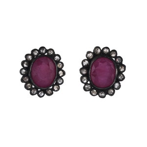 May include: A pair of silver earrings featuring a red oval gemstone set within a halo of smaller white gemstones.