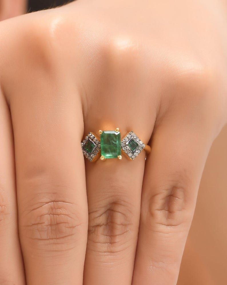 Close-up of ring worn on hand, showing prong-set emerald center detail