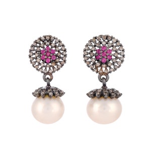 May include: A pair of silver earrings with a pearl drop and a circular design featuring small diamonds and pink gemstones.