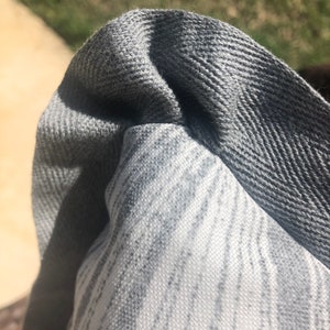 Pu&ograve; includere: Primo piano di un tessuto a motivi grigi e bianchi con un bordo in tessuto grigio. Il bordo ha un motivo a spina di pesce.