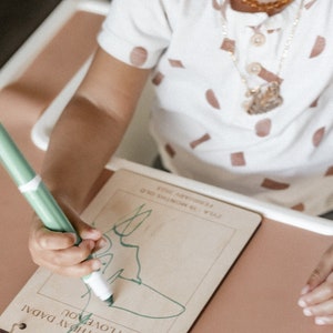 May include: A child draws on a wooden board with a green marker. The board has the text "Happy Birthday Dadal I Love You" and "Zyla is now 18 months old February 2023".