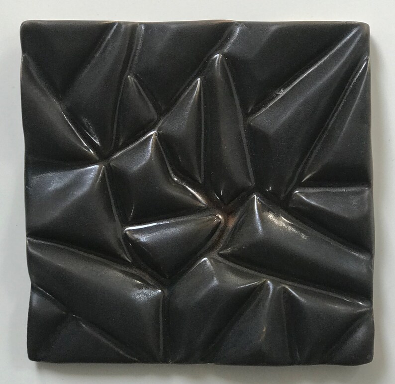 May include: A black ceramic tile with a textured, geometric pattern. The tile has a glossy finish and a three-dimensional design.
