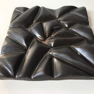 May include: A black ceramic wall sculpture with a geometric design. The sculpture is made of many small triangles that are arranged in a random pattern. The surface of the sculpture is smooth and shiny.