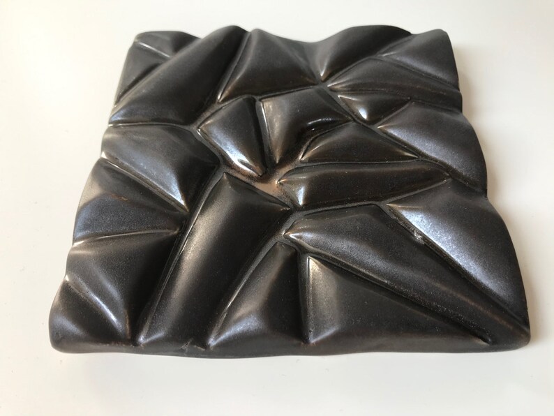 May include: A black ceramic wall sculpture with a geometric design. The sculpture is made of many small triangles that are arranged in a random pattern. The surface of the sculpture is smooth and shiny.