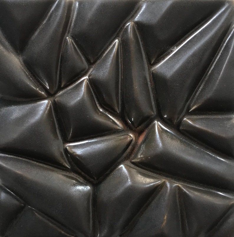 May include: A black ceramic tile with a textured, geometric pattern. The tile has a glossy finish and a three-dimensional design.