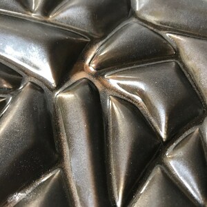 May include: Close-up of a black, textured surface with a geometric pattern. The surface is made of a material that appears to be rubber or plastic. The pattern is made up of a series of raised triangles.