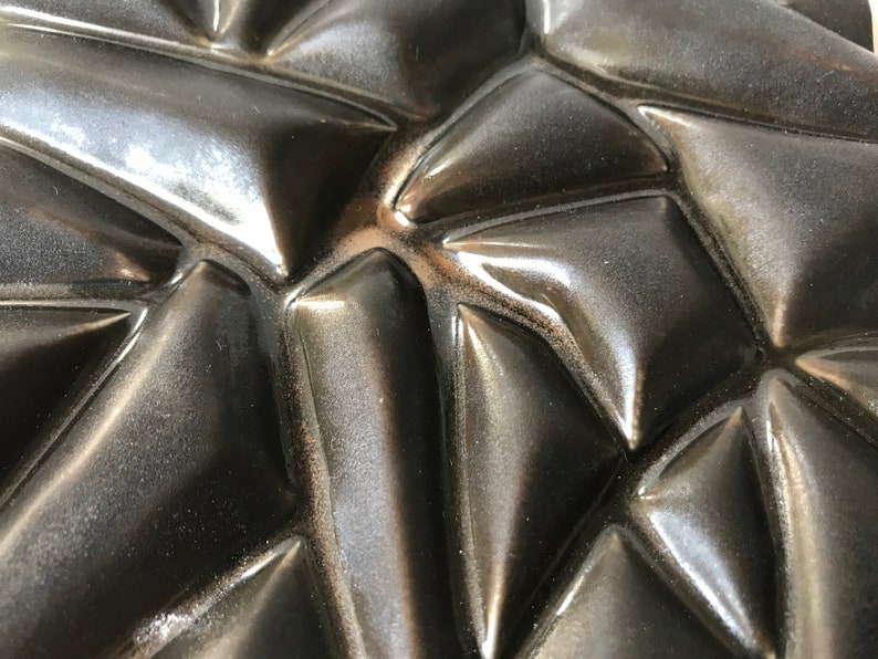 May include: Close-up of a black, textured surface with a geometric pattern. The surface is made of a material that appears to be rubber or plastic. The pattern is made up of a series of raised triangles.