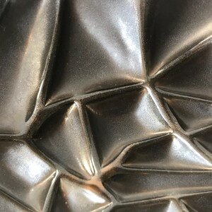 May include: Close-up of a dark gray, textured surface with a geometric pattern. The surface is made of a material that appears to be ceramic or metal.