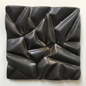 May include: A black ceramic tile with a textured, geometric pattern. The tile has a glossy finish and a raised, three-dimensional design.