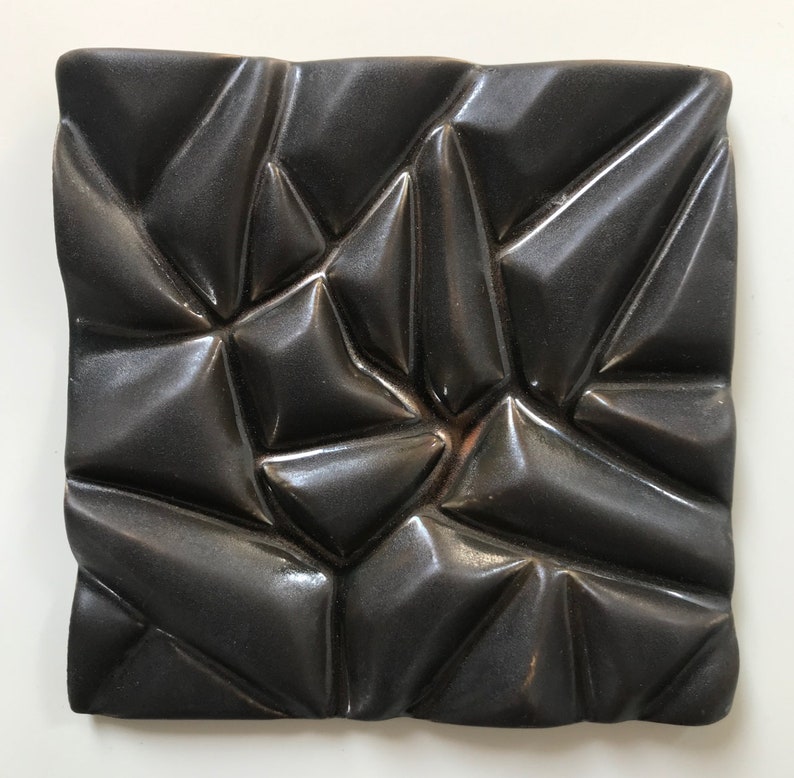 May include: A black ceramic tile with a textured, geometric pattern. The tile has a glossy finish and a raised, three-dimensional design.