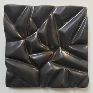 May include: A black ceramic tile with a geometric pattern of raised triangles. The tile has a glossy finish and a textured surface.