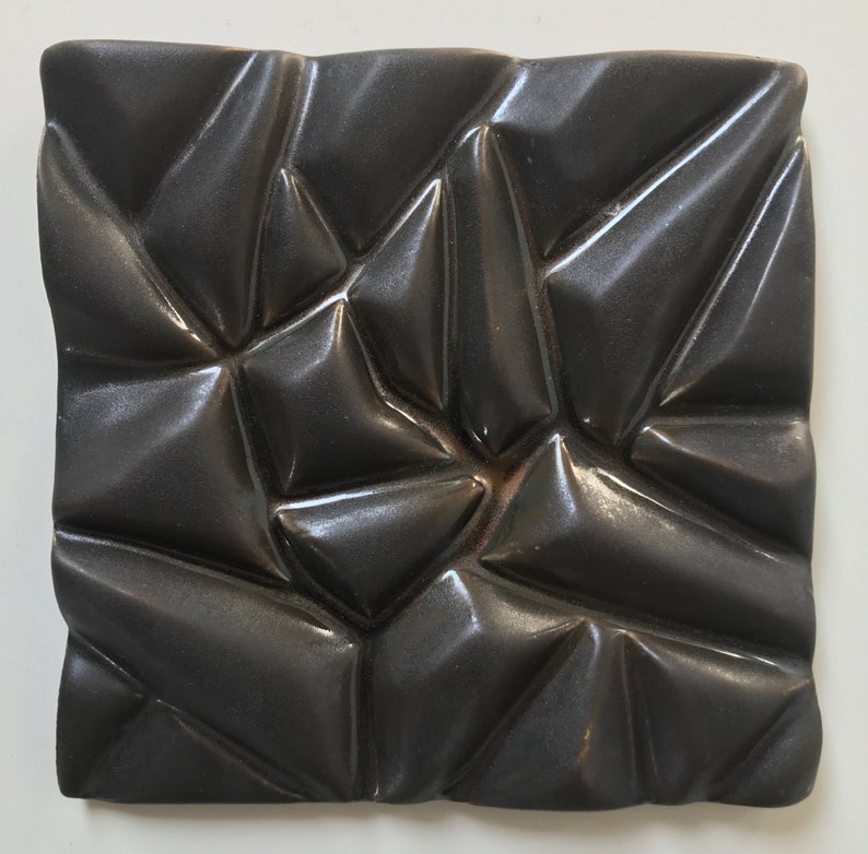 May include: A black ceramic tile with a geometric pattern of raised triangles. The tile has a glossy finish and a textured surface.