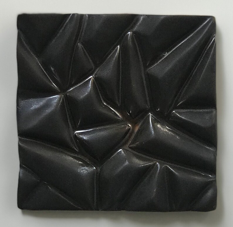 May include: A black ceramic tile with a textured, geometric pattern. The tile has a glossy finish and a raised, three-dimensional design.