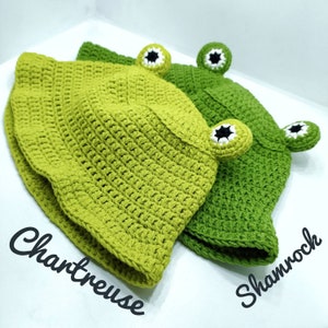 Op de afbeelding: Twee gehaakte bucket hats met kikkerogen met witte en zwarte details. De ene hoed is chartreuse en de andere is klavergroen. De tekst Chartreuse staat bij de lichtere hoed en Shamrock staat bij de donkerdere hoed.