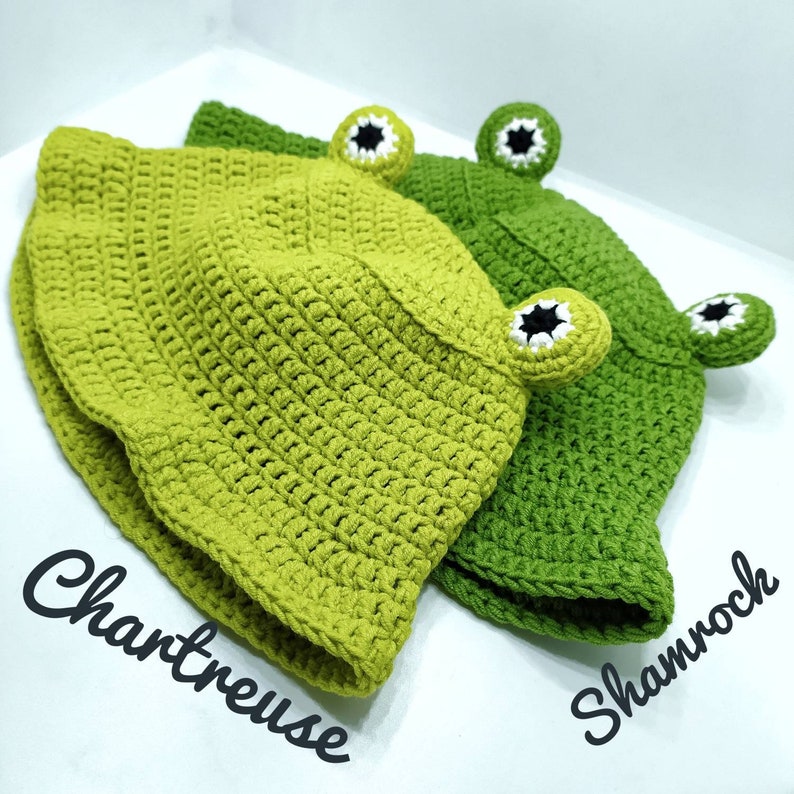 Op de afbeelding: Twee gehaakte bucket hats met kikkerogen met witte en zwarte details. De ene hoed is chartreuse en de andere is klavergroen. De tekst Chartreuse staat bij de lichtere hoed en Shamrock staat bij de donkerdere hoed.
