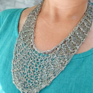 Puede incluir: Un collar metálico ancho de tono plateado con una intrincada construcción de malla abierta. La pieza tiene una apariencia texturizada similar a una red con una caída flexible que se contornea alrededor del cuello, mostrando un patrón de eslabones.
