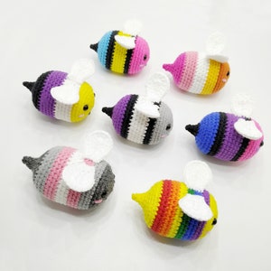 Peut inclure: Sept peluches d'abeilles au crochet, chacune avec un schéma de couleurs différent représentant un drapeau de fierté différent. Les abeilles ont des yeux noirs et des ailes blanches.