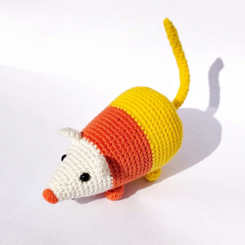 Pu&ograve; includere: Un topo giocattolo realizzato all'uncinetto con un design a blocchi di colore, caratterizzato da una testa bianca, una sezione centrale arancione e una parte posteriore con coda gialla. Il piccolo peluche ha due occhi a perla neri e un naso.