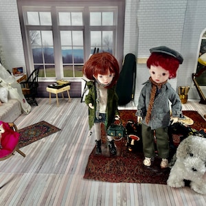 May include: Two ball-jointed dolls with red hair stand on a dark red rug in a miniature room. One doll wears a green jacket and carries a small green bag, while the other wears a gray jacket, a cap, and a scarf. A small white dog figure sits nearby.