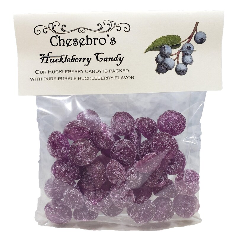 May include: A clear plastic bag filled with purple huckleberry candies. The bag has a white label with the text "Chesbro's Huckleberry Candy" and "Our huckleberry candy is packed with pure purple huckleberry flavor."