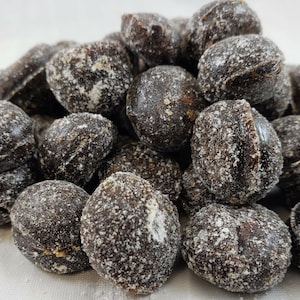 May include: A pile of dark brown, round candies covered in a white, powdered sugar coating.