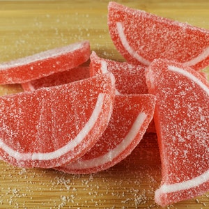 May include: A close-up of red and white gummy candies shaped like watermelon slices. The candies are covered in a white sugar coating.