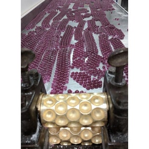 May include: A close-up of a candy making machine with a gold roller and a large amount of pink candy on a metal surface.