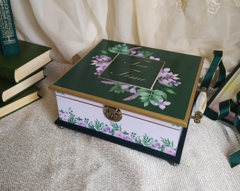 Puede incluir: Una caja de té decorativa con tapa verde adornada con diseños florales y de hojas, y la inscripción "Tea Time". La caja tiene un cuerpo blanco con detalles florales, un borde dorado y un asa decorativa.