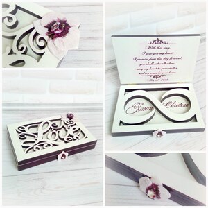 May include: White wooden ring box with a cutout design of the word "love" and an infinity symbol with the names "Jason" and "Christine" inside. The box is decorated with small white flowers and has a purple inscription on the inside lid that reads "With this ring, I give you my heart. I promise from this day forward, you shall not walk alone. May my heart be your shelter, and my arms be your home. May 27, 2018."