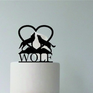 Könnte beinhalten: Schwarze Silhouette von zwei Wölfen, die sich gegenüberstehen und heulen, innerhalb einer Herzform mit dem Wort "WOLF" darunter. Die Silhouette befindet sich auf einem weißen Kuchen.