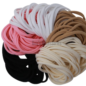 Puede incluir: Una colección de 100 gomas para el pelo suaves y elásticas en cinco colores: negro, blanco, rosa, beige y marrón. Las gomas para el pelo están dispuestas en un círculo, con los colores alternando.