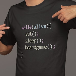 Peut inclure: Un t-shirt noir avec un extrait de code imprimé dessus. Le code est le suivant : "while(alive){ eat(); sleep(); boardgame(); }"