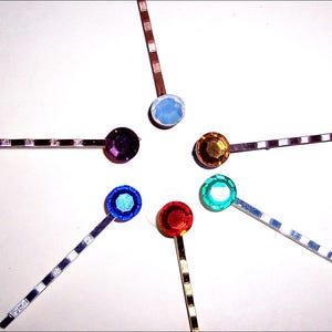May include: Six hair clips with different colored rhinestones. The clips are silver, gold, and copper colored. The rhinestones are purple, blue, green, red, gold, and white.