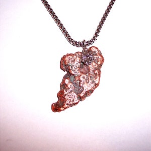 May include: A silver chain necklace with a pendant made of a rough, irregular piece of copper. The copper has a reddish-brown color and a textured surface.
