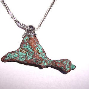 May include: A silver chain necklace with a pendant made from a rough, irregular piece of copper with a green patina. The pendant is attached to the chain with a silver ring.