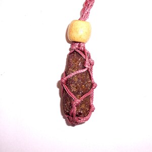 May include: A dark red stone wrapped in a pink cord necklace with a wooden bead.