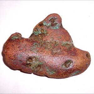 May include: A large, irregularly shaped piece of copper ore with a reddish-brown color and green patina. The ore has a rough, textured surface with several small holes.