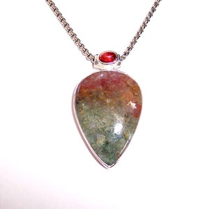 May include: A silver chain necklace with a teardrop-shaped pendant featuring a multi-colored stone with green, brown, and red hues. A small red gemstone is set at the top of the pendant.