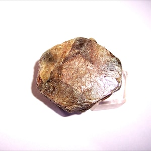 May include: A large, brown, and green gemstone with a rough, irregular shape. The gemstone has a metallic sheen and is likely a raw, uncut crystal.