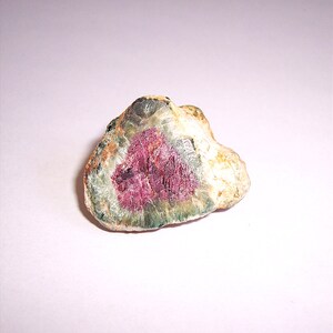 May include: A rough, irregularly shaped, light brown, green, and pink gemstone with a pink center.