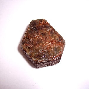 May include: A dark brown, faceted gemstone with a hexagonal shape. The gemstone has a rough, textured surface and appears to be translucent.